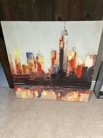 Full view of the square canvas oil painting showing colorful abstract city skyline with strong emphasis on red, yellow, and black.