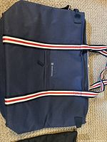 Front view of navy blue cooler bag showing red, white and blue striped handles and zipper closure.