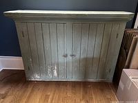 Front view of the sideboard hutch with two closed doors showing distressed light green paint and natural wear at the bottom edges.