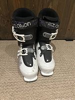 Front view of the pair of black and white Salomon SPK ski boots showing two white buckles each and black liner inside.