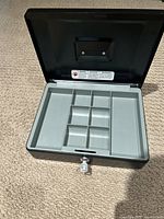 Open cash box showing gray inner organizer tray with several sections for bills and coins.
