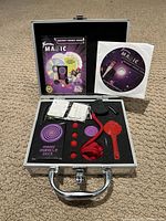 Open metal case showing foam insert holding magic accessories, booklet, and DVD