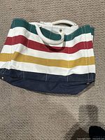 Tote bag showing exterior with horizontal stripes in green, red, yellow, white, and navy base with white handles.