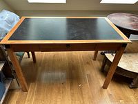 Overall front view of brown wood desk with black inset top and wooden legs.