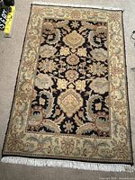 Full top view of the traditional wool area rug showing black central field with floral motifs and beige border with fringe.