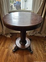 Wooden round vintage accent table showing tabletop and single-column base with four curved feet.
