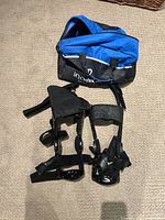Photo showing two black knee braces and blue carrying bag on carpeted floor