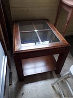 Photo of a 1970's wooden coffee table with clear glass insert top and lower storage shelf shown in room environment.