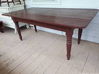 Full front view of red painted harvest table on porch floor
