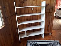 White wood shelving unit placed against wood-paneled wall, showing the entire unit with 5 shelves and divided bottom shelf.