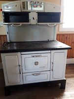 Front view of full cook stove showing white enamel body, mirrored upper doors and black cast iron top