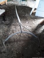 Full length of the vintage wooden buggy shaft with curved metal details attached at the end, laying on dirt ground inside a shed.