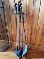 Four vintage fireplace tools with twisted metal handles topped with round knobs on a triangular stand set against wood paneling