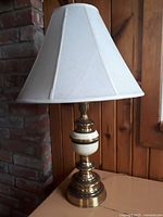 Full view of the cream and gold metal lamp with white fabric shade, highlighting the heavy metal base and hexagonal shade shape.