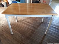 Photo showing the oak kitchen table with polished oak top and white turned legs, placed on wooden floor indoors.