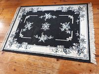 Photo showing rectangular navy area rug with floral pattern and white fringe laid on wooden floor.