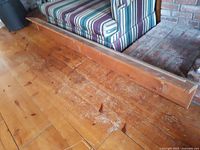 Long pine wood plate rail shelf placed on wooden floor in front of a striped sofa and brick fireplace.