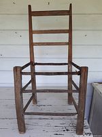 Front view of a primitive handmade wooden ladderback chair showing three horizontal slats on the backrest. The chair frame is worn and lacks the seat, which needs to be replaced with rushing or rope.