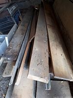 Long wood planks stacked on one another with some dirt and wear visible, mostly pale pine wood.