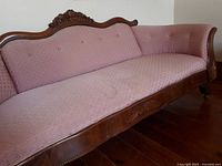 Full angled view of pink upholstered settee with carved wooden frame and rose details on crest rail.