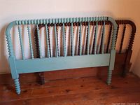 Photo of a light blue wooden headboard and a dark natural wood footboard with spindle/turned design against wall on wooden floor.