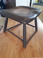 View of the old handmade wooden stool showing the worn square seat and triangular leg supports