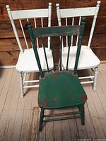 Three vintage wooden chairs, two white and one green, showing varying degrees of wear and paint chipping.