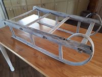 Primitive wooden child's sleigh placed on a wooden table showing its construction and condition.