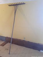 Full view of the grain fork leaning against a wall, showing the long handle and fork tines horizontally at the top