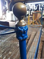 Close-up of the brass knob ornament atop a blue painted metal post of the bed frame showing its vintage ornate style.