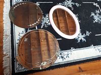 Three vintage mirrors on a rug on wooden floor: two round etched mirrors (16" and 18") and one oval pink bevel glass mirror with a pink frame (20" x 15").