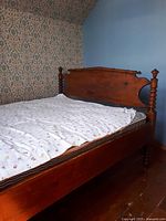 Full side view of vintage pine spool bed with mattress and floral sheet covering, showing the headboard, side rails, and turned bedposts.