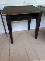 Side view of vintage wooden teacher's desk showing square tapered legs and chipped greenish-brown paint.