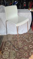 Photo showing side angle of the white molded plastic bar stool with chrome sled legs on a patterned rug.