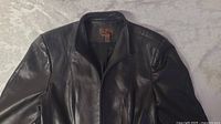 Front view of black leather ladies jacket with collar and zip closure laid flat