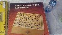 Photo of the deluxe solid wood labyrinth game in its box with maze and metal ball visible, next to a water bottle for scale.
