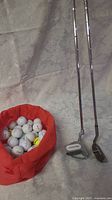 Two Tommy Armour golf clubs (chipper and putter) and a red bag with multiple golf balls.