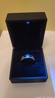 Men's tungsten ring displayed inside a black velvet-lined presentation box with the lid open.