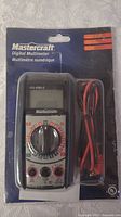 Photo shows a new in box Mastercraft digital multimeter with red and black test leads coiled, still sealed in original blue card packaging.