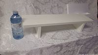 White straight line wall shelf shown with a water bottle for scale on a floral patterned fabric surface