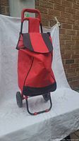Front view of red and black fabric shopping trolley showing flap closure, handle, and wheels