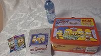 Unopened Simpsons trading card packs with character graphics and Simpsons first season DVD case.