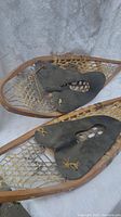 Front view of one snowshoe showing wooden frame, rawhide lacing, and leather foot binding