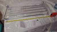 Chrome 24 inch towel holder shelf on table with measuring tape showing length, still in protective plastic wrap.