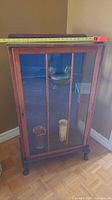 Full front view of the vintage wooden curio cabinet with glass door showing interior with one glass shelf and wooden feet.