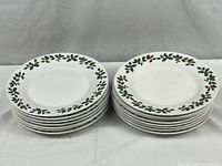 Two stacks of white ceramic plates with green holly and red berries pattern around the rim, showing a total of 15 plates.