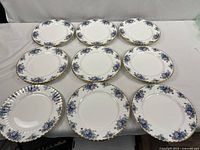 Top-down photo of 16 dinner plates arranged in a grid on a white cloth showing floral pattern and gold trim