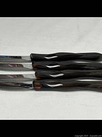 Four black-handled serrated knives laid out, showing handles and partial blades.
