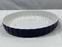 Side view of the blue exterior and white interior of the ceramic pie dish showing fluted edges and smooth finish.