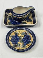 Ceramic handmade pourer set with rectangular platter and round dish, all featuring blue grape cluster design on cream and blue background.